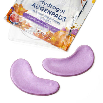 Zwei glitzernde, lila Hydrogel-Augenpads vor der Mystic Pumpkin Verpackung mit Kürbis- und Feigen-Motiv.