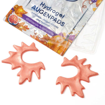 Zwei blattförmige, glitzernde orangefarbene Hydrogel-Augenpads vor der Mystic Pumpkin Produktverpackung.