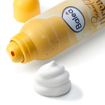 Gelbe Balea Bodylotion Mousse Dose mit weißem Schaumklecks auf weißem Hintergrund.