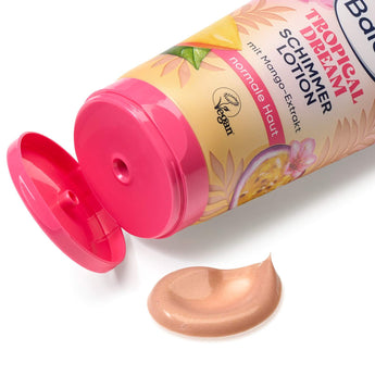 Balea Tropical Dream Schimmer-Bodylotion in einer Tube mit pinkem Klappdeckel und einem Klecks gold-schimmernder Creme.