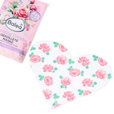 Herzförmige Balea Dekolleté-Tuchmaske mit weißem Stoff und aufgedrucktem rosa Rosenmuster neben der pinken Produktverpackung.