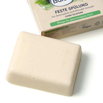 Cremefarbenes Stück fester Balea Conditioner vor der Verpackung mit Avocado- und Mandel-Design.