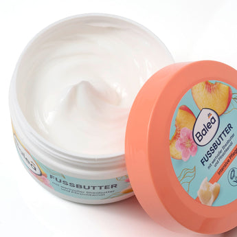 Geöffneter Tiegel Balea Fußbutter mit weißer Creme, pfirsichfarbenem Deckel und Pfirsich-Design auf weißem Hintergrund.