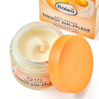 Offener Glastiegel mit Balea Q10 Energy Gesichtscreme, cremiger Textur und orangefarbenem Deckel vor der Produktverpackung.