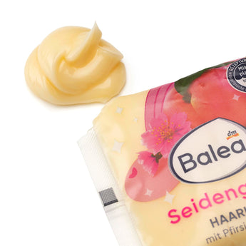 Balea Seidenglanz Haarkur Sachet mit Pfirsich-Design und einem Klecks cremiger, gelber Haarpflege auf weißem Hintergrund.